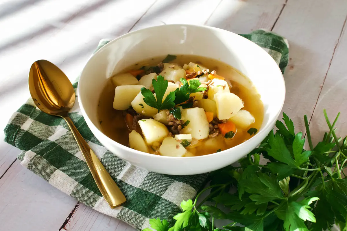 Finnish minced meat soup in a white bowl with potatoes, carrots and parsnips visible, garnished with fresh parsley
